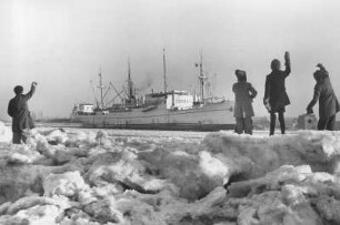 Hamburg-Ottensen. Elbe bei Neumühlen im Winter. Spaziergänger winken einem auslaufenden Frachtschiff zu