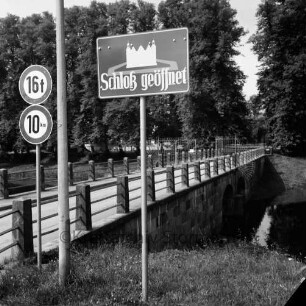 Schlossbrücke: mit Gittertor: im Vordergrund Hinweisschild "Schloß geöffnet", Lampenmast, Verkehrsschilder: Schlossgraben: hinten Schlossinsel