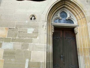 Stiftskirche-Ansicht von Westen-nördliches Portal mit abgetrepptem spitzbogigem Gewände und beidseitigen plastischen Schrecköpfen-nördlich eine Nische mit plastischem (Baumeister-) Kopf