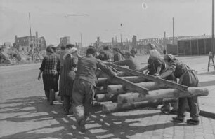 Berlin. Aufbauhelfer transportieren Bahngleise mit Holzschwellen auf einer Straße in Trümmerlandschaft
