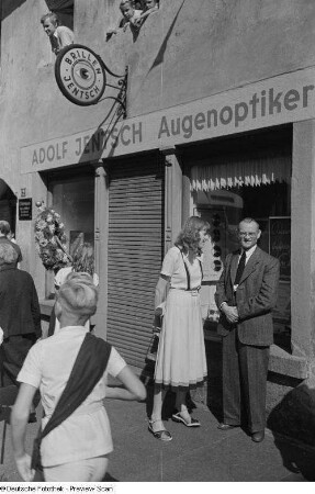 Renate Rössing und Herr Böttger am Rande des Auszugs der Kinder beim Kamenzer Forstfest stehend, im Hintergrund das Geschäft des Augenoptikers Adolf Jentsch
