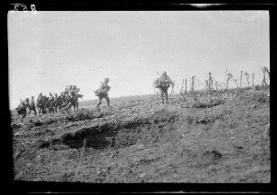 Übungsgelände I bei Mouzon (Dep. Ardennes, Frankreich): Soldaten mit Stahlhelm und Marschgepäck auf einem kahlen, leicht ansteigenden Feld neben einem Drahtverhau, im Vordergrund eine Grube ("Vorgehen der Infanterie")