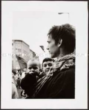 Junger Mann mit Baby auf dem Arm bei einer Demonstration (Altersgruppe 18-21)