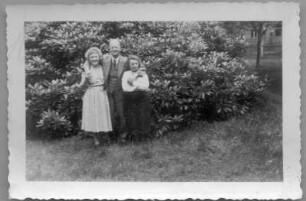 Etha Richter mit einem Ehepaar, vor einem Rhododendronstrauch stehend