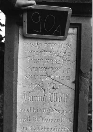 Grabstein 90 (Index: 100080556) Material: Sandstein, weiße Marmorplatte Zustand: Platte mehrfach gesprungen Maße HxBxT: 142x50x26 cm Beschreibung: Stele, Giebel m. stilisiert. Eckakroteren, rechteckige Schriftplatte Symbolik: Mohnkapseln, Blätter, Voluten im Giebel: Grabstein 90A