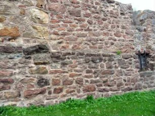 Kirchhofmauer im Südsüdwesten mit Werksteinen im Mauersteinverband sowie Brüstungsversatz (des ehemaligen Wehrgangs) über Kirchhof