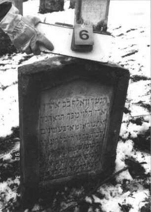 Grabstein 6 (Index: 99608690) Material: Sandstein Zustand: leicht bis mittelstark verwittert Maße HxBxT: 73x51x13 cm Beschreibung: Stele mit flachem Spitzgiebel, vertiefter Textteil in gleicher Form Besonderheit: Kindergrab: Grabstein 6