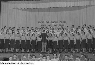 Auftritt eines am Bezirksausscheid der Volkskunstgruppen 1954 teilnehmenden Chores, im Vordergrund der Chorleiter und ein Orchester