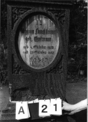 Grabstein 21 (Index: 99792914) Material: Sandstein und Marmor Zustand: beschädigt Maße HxBxT: 162x52x34 cm Beschreibung: Stele, Sockel profiliert, Giebel mit Akroter, Schriftfeld eingetieft, stehendes Oval, eingesetzte Textplatte Symbolik: Efeublätter Besonderheit: Schrift vergoldet: Grabstein 21A