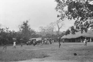 Ankunft in Namgaru : Expeditionsträger bei der Ankunft in Namgaru. Savannenlandschaft mit Bäumen, Hütte, Automobil und Expeditionsteilnehmern.
