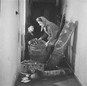 Mutter und Kind in einem Hausflur mit gesammeltem Feuerholz