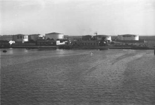 Öltanks : Sueskanal. Blick vom Wasser aus auf Öltanks und Gebäude