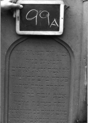 Grabstein 99 (Index: 99937115) Material: Sandstein Zustand: gut Maße HxBxT: 170x61x30 cm Beschreibung: ädikulaartige Stele mit Halbsäulen, profilierter Sockel, Giebel mit stilisierten Eckakroteren, Schriftfeld eingetieft mit Rundbogenabschluß Symbolik: Maßwerk mit herabhängenden Herzen, Voluten und Efeuranken im Giebel: Grabstein 99A