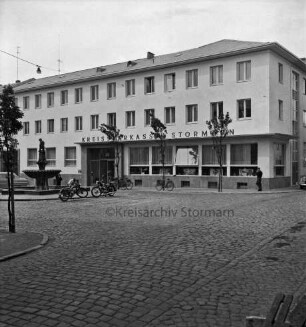 Kreissparkasse Stormarn: Markt: Hauptstelle: links Altbau nach Umbau, rechts Erweiterungsbau Ecke Hagenstraße: vor Einweihung: Außenaufnahme mit Firmenname: davor Markt mit Kopfsteinpflaster, junge Bäume: Gänselieselbrunnen: Fahrräder, Motorräder