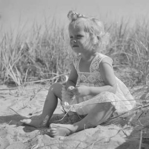 Kleines Mädchen mit Kleid sitzt am Strand